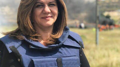 Beloved journalist and martyr Shireen Abu Akleh smiling at the camera, wearing a blue press vest.