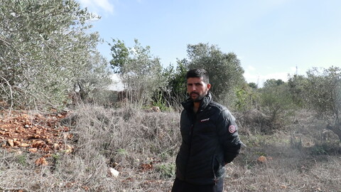 Man wearing black standing in front of his farm in the border town of Dhayra, South Lebanon. He is surrounded by burnt trees and grass impacted by Israel's White Phosphorus attacks. 