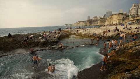 Dozens of people swim in Dalieh as the waves crash on the shore. 