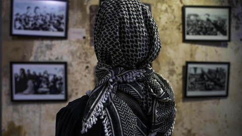 Woman wearing keffiyeh looks at photographs