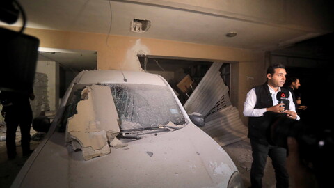 Reporter stands next to blast-damaged car