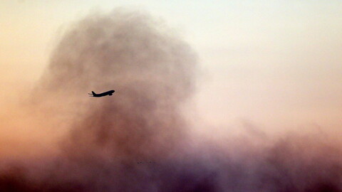 An airplane flies over Beirut's southern suburbs of Dahye, with plumes of smoke rising in the background from ongoing Israeli bombardment.