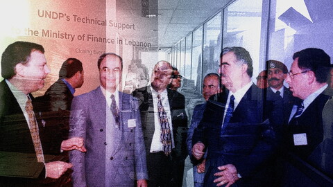 A composite photo. A group of five men in suits are huddled together in the foreground deep in discussion. In the background is a hallway with stacks of loose papers, merged with a large poster that reads: "UNDP's Technical Support to the Ministry of Finance in Lebanon: Closing Event."