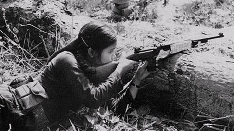 A black-and-white photo features a southern Vietnamese female guerrilla fighter pointing her rifle with determination, embodying the resilience of those who fought for their homeland.