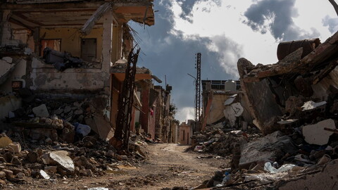 Rubble-lined street between heavily damaged buildings in the village of Blida, south Lebanon, with collapsed concrete and exposed steel.