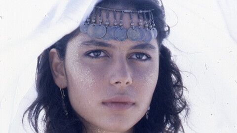 Close up of a woman in headdress and glitter staring into the distance.