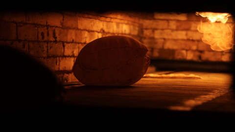A loaf of Arabic bread inflates inside an oven. Fire seen in the background.