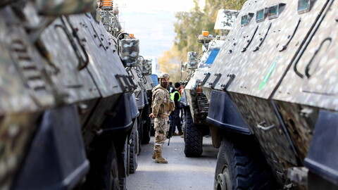 A soldier stands between military vehicles on a street, conveying tension and readiness.
