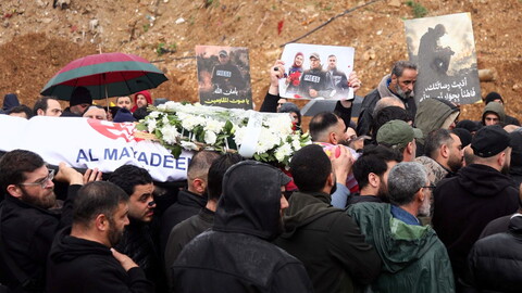 A crowd of mourners carries a coffin draped with an Al Mayadeen flag and covered in white flowers during a funeral in Dahieh, Beirut, while others hold photos of slain journalists, Ali Shoeib, Fatima and Mohammad Ftouni..