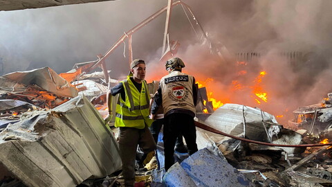 First responders stand amid burning rubble in what seems to be a collapsed building.