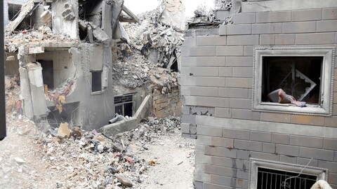 Rubble from collapsed buildings fills a narrow alley, with debris strewn across.
