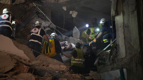 Rescue workers carry a person on a stretcher through rubble at night, using flashlights to navigate the collapsed building debris in Beirut, Lebanon.