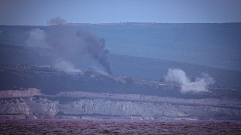 Distant hills with puffs of dark smoke rising into a clear sky.