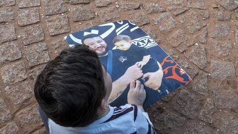 A child holding a photo of a man carrying a child. 