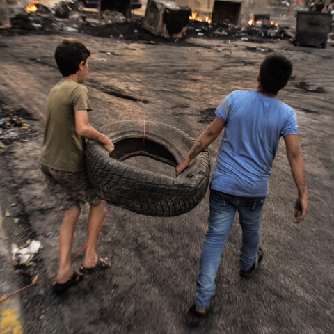 Two young boys carry a tire at a roadblock reinforced by burning dumpsters. Beirut, Lebanon. October 18, 2019. (Mouran Mattar/Fawra)