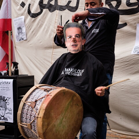 A protester wears a mask depicting central bank governor Riad Salameh’s face while getting a “haircut” in front of the Central Bank.