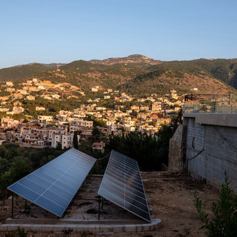 Two rows of solar panels installed on land surrounding villa that oversees a village. 