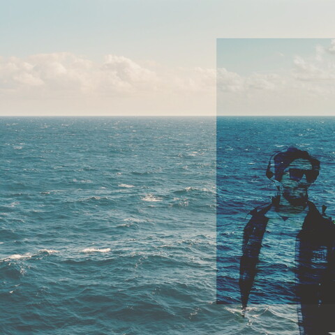 Image of the Mediterranean sea in the background, and a young man in the foreground.