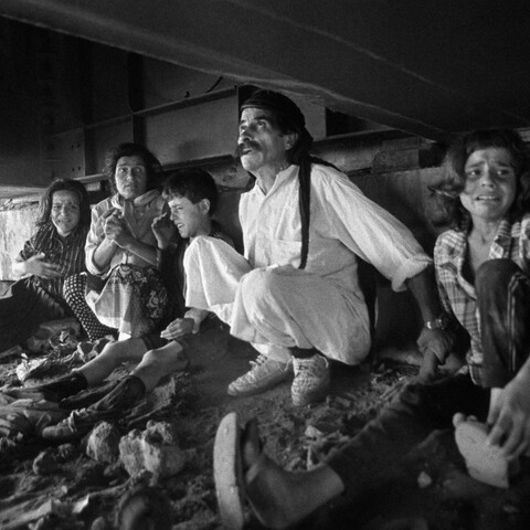 A terrified family taking refuge from shelling under a metallic bridge.