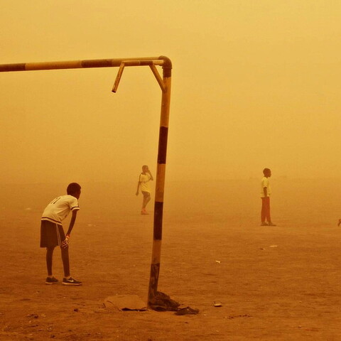 Kids playing football on the sand in the middle of a sandstorm that colors the entire photo golden-yellow.