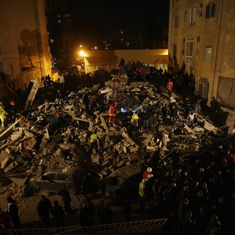 First responders search the ruins of a collapsed building at night.