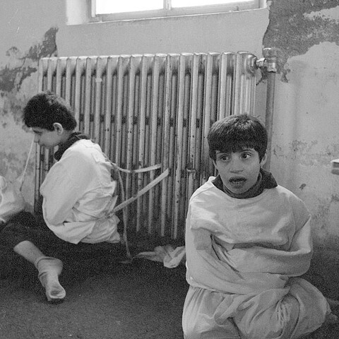 A black and white photograph showing two children fettered to a radiator at the psychiatric hospital of Deir El-Salib in Deir El-Qamar, Lebanon.