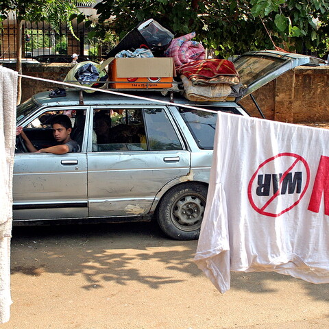 A young man drives a car loaded with his belongings past a park. 