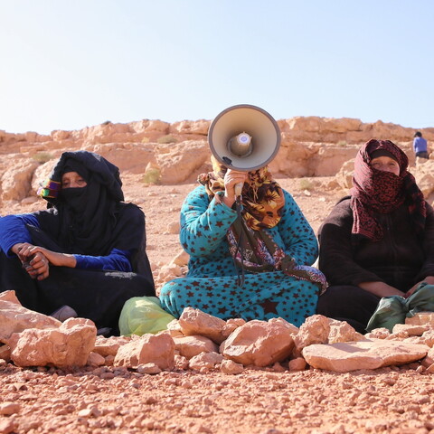 مجموعة من ست نساء أمازيغيات يجلسن على الأرض كتفًا لكتف. جميعهن لديهن شعر ووجوه مغطاة جزئيا؛ واحدة منهن تتحدث في مكبر الصوت.