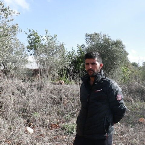 Man wearing black standing in front of his farm in the border town of Dhayra, South Lebanon. He is surrounded by burnt trees and grass impacted by Israel's White Phosphorus attacks. 