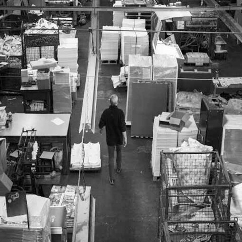 A person walks through a warehouse filled with stacks of paper, boxes, and various materials.