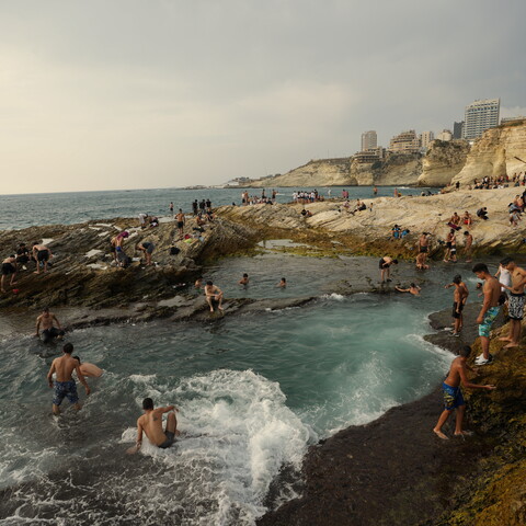 Dozens of people swim in Dalieh as the waves crash on the shore. 