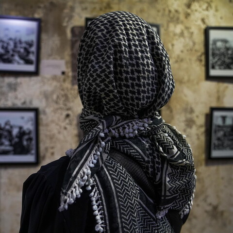 Woman wearing keffiyeh looks at photographs