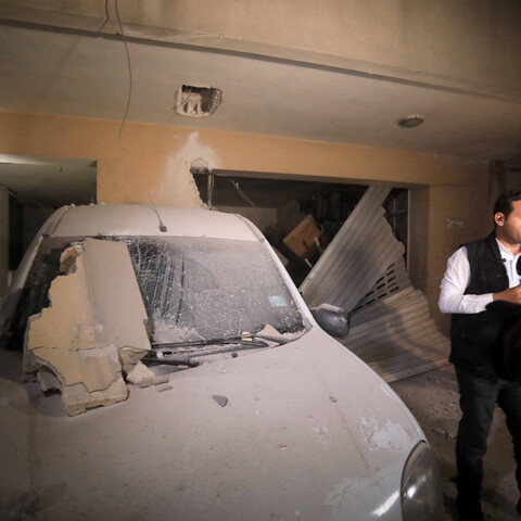 Reporter stands next to blast-damaged car