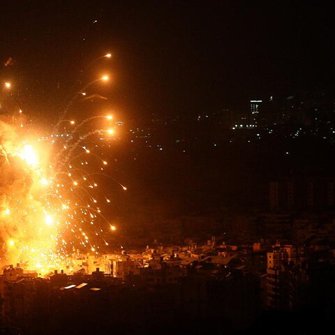 A nighttime airstrike causes an explosion over a dark town.