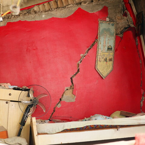 A collapsing red wall and destroyed furniture. A piece of tapestry showing the al-Aqsa Mosque still hangs on the red wall.