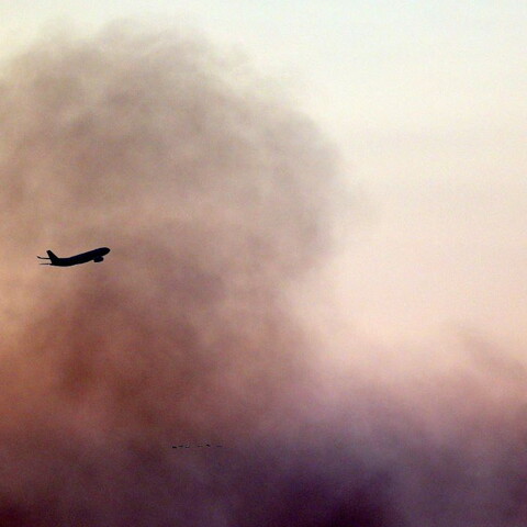 An airplane flies over Beirut's southern suburbs of Dahye, with plumes of smoke rising in the background from ongoing Israeli bombardment.