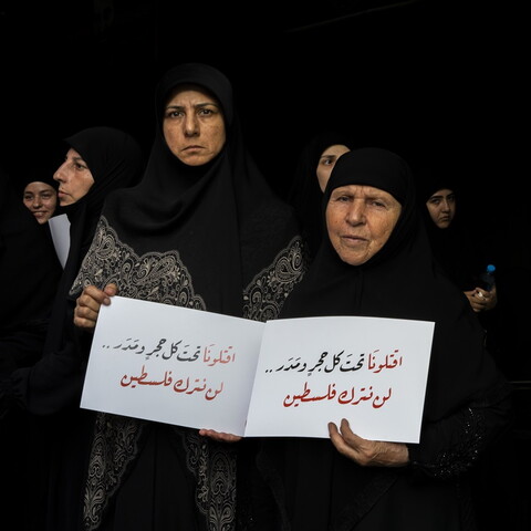 Two veiled women stand facing the camera, other women stand behind them. All are wearing black.
