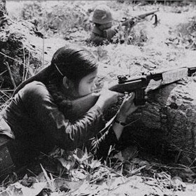 A black-and-white photo features a southern Vietnamese female guerrilla fighter pointing her rifle with determination, embodying the resilience of those who fought for their homeland.