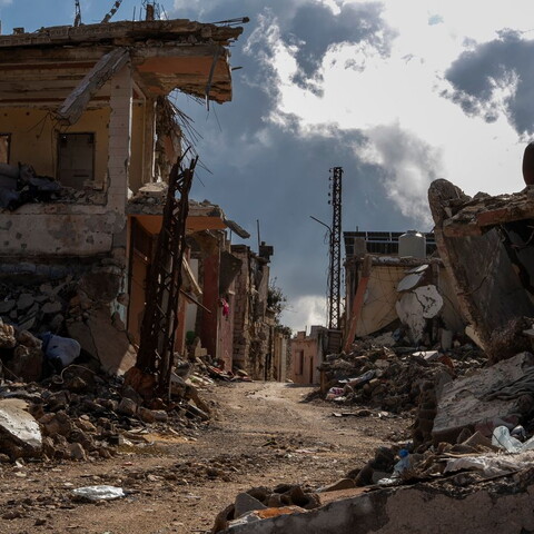 Rubble-lined street between heavily damaged buildings in the village of Blida, south Lebanon, with collapsed concrete and exposed steel.