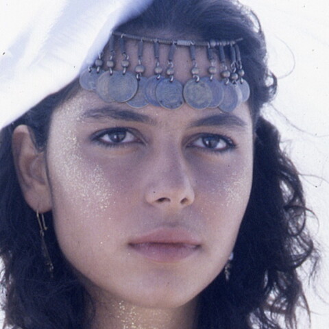 Close up of a woman in headdress and glitter staring into the distance.