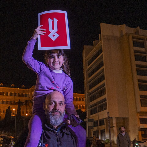 A demonstrator carries his daughter on his shoulders; she carries a poster in Arabic that reads: "No."