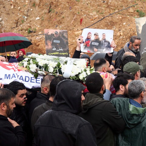 A crowd of mourners carries a coffin draped with an Al Mayadeen flag and covered in white flowers during a funeral in Dahieh, Beirut, while others hold photos of slain journalists, Ali Shoeib, Fatima and Mohammad Ftouni..