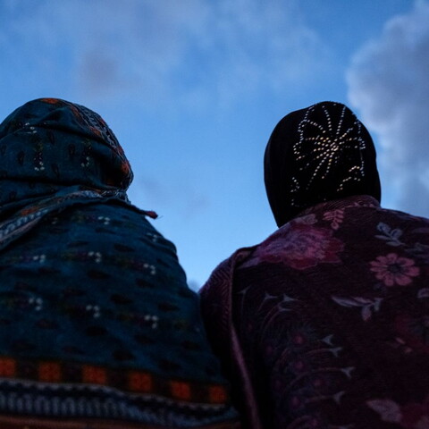 Two women wearing hijab stand under a clear blue sky.