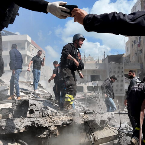 Civil Defense and other responders join forces to rescue people trapped under the rubble following the Hay al-Raml/al-Raml neighborhood strike in Sur. A Civil Defense member’s hand is seen taking a cellphone from another, as people check on one another in the aftermath of the strike. It is one of more than 160 strikes—the largest Israeli wave of fire attacks on the country since the beginning of the genocidal campaign on Palestine and Lebanon in October 2023. 