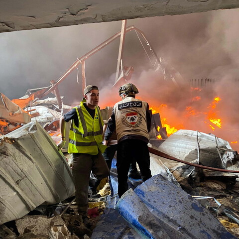 First responders stand amid burning rubble in what seems to be a collapsed building.