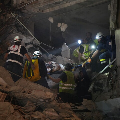 Rescue workers carry a person on a stretcher through rubble at night, using flashlights to navigate the collapsed building debris in Beirut, Lebanon.