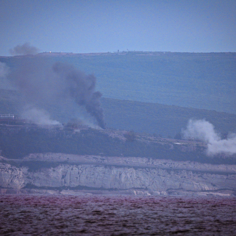 Distant hills with puffs of dark smoke rising into a clear sky.