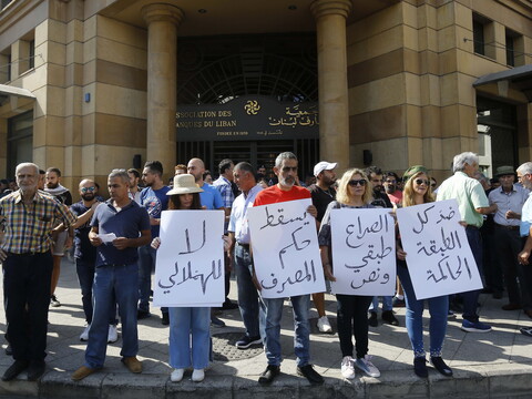 Protesters standing in front of the headquarters of the Association of Banks of Lebanon, carrying signs that read “Down with the rule of the banks.”