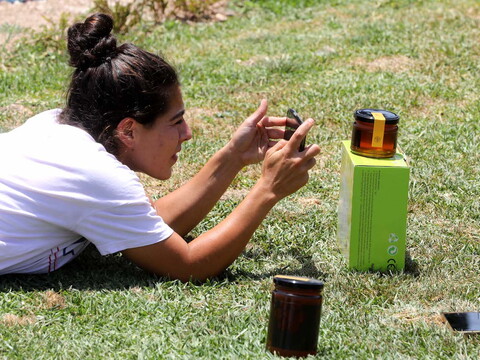 Moné Makkawi lies on the grass to photograph a jar of honey.