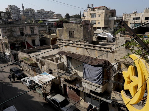 A picture of a street in Qobbeh, Tripoli. An asphalt road can be seen, surrounded by worn down grey buildings, many electricity cables, and a yellow moon and star sign.